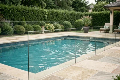 Barrière de piscine en verre transparent installée autour d'une piscine extérieure moderne dans un jardin soigné